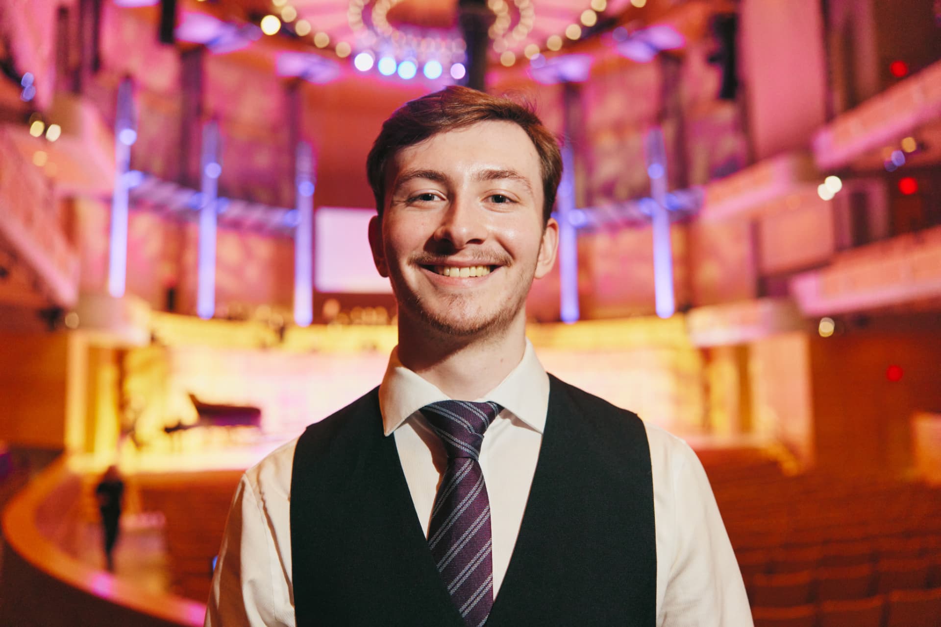 A smiling hospitality worker standing in a warmly lit auditorium